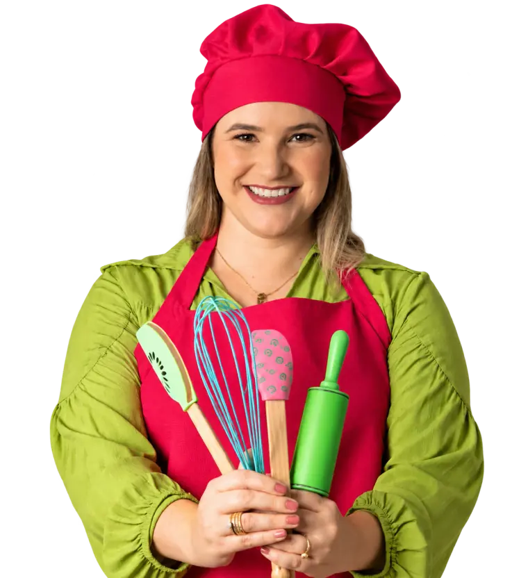 Lígia de touca e avental de cozinha, segurando espátula, fouet e rolo de massa coloridos